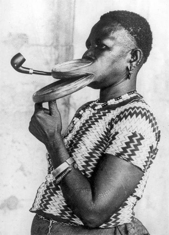 Madam Gustika of the Duckbill tribe smoking a pipe with an extended mouthpiece for her lips during a show in a circus.
